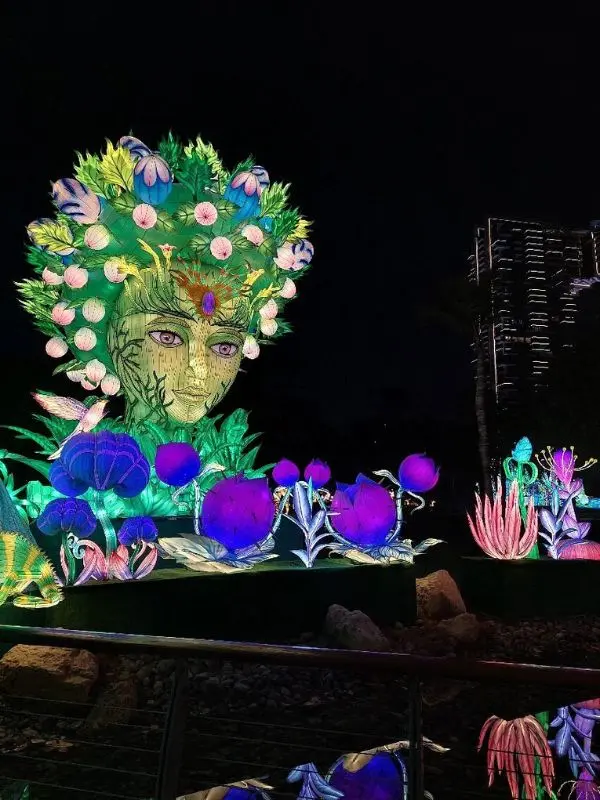 A glowing green and purple sculpture surrounded by illuminated flowers at Dubai Garden Glow.
