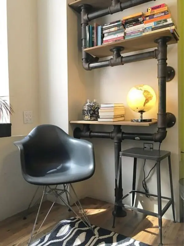A small reading nook at American Dream Hostel with a black chair, pipe shelving, and a glowing globe lamp.