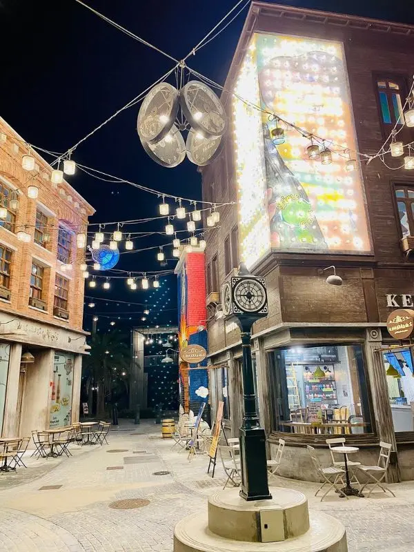 A night scene at La Mer with string lights, decorated buildings, and a street clock in the center.