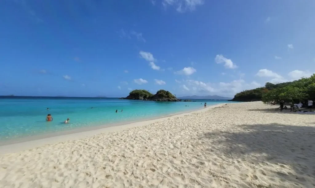 Soft white sand meets bright turquoise water with small islands offshore at Trunk Bay, US Virgin Islands.