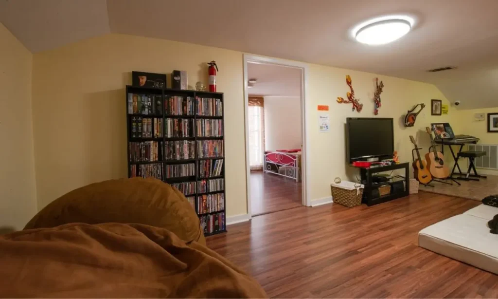 A music-themed lounge at Auberge NOLA Hostel with a TV, guitars, DVD shelves, and a keyboard.