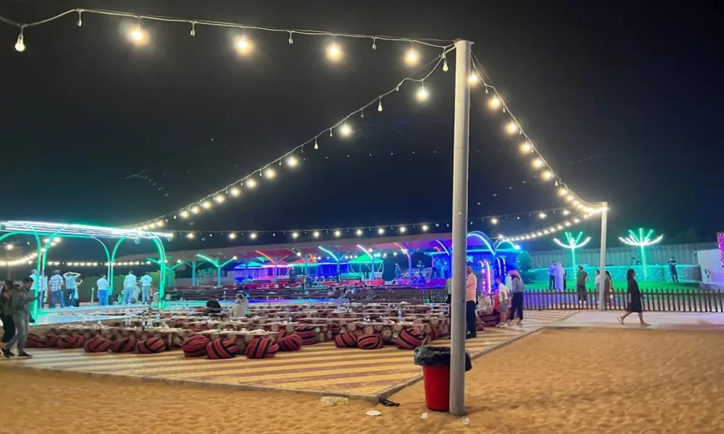 A night view of a Desert Safari camp with string lights and seating arranged on the sand.