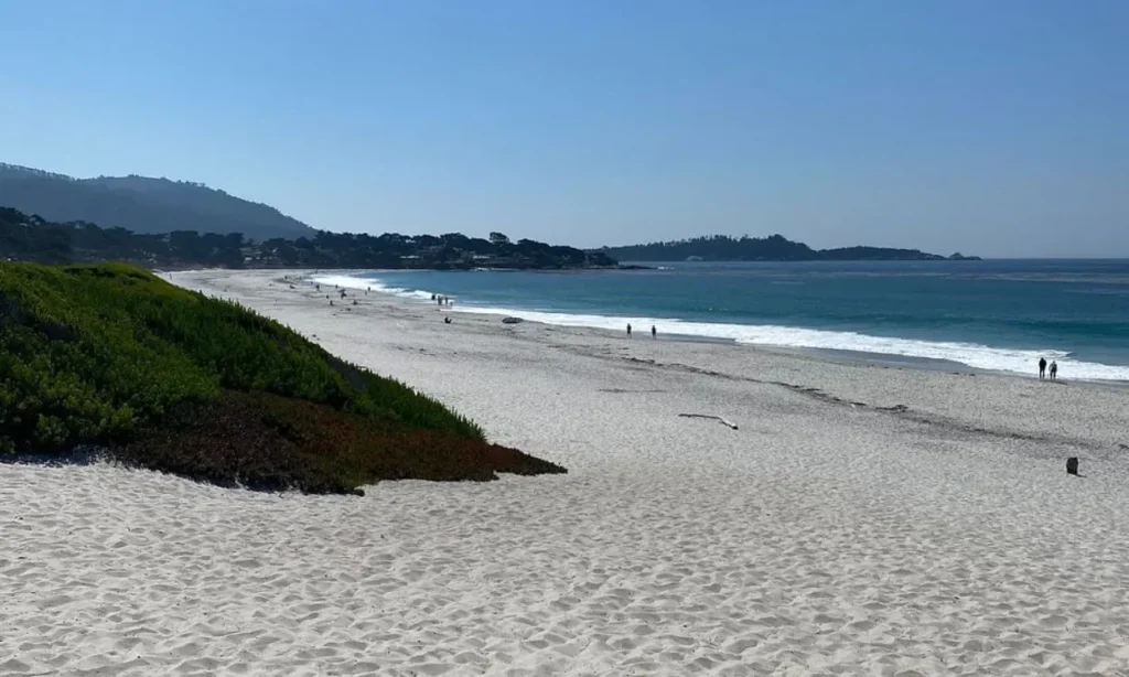 Smooth white sand and gentle waves stretch along Carmel Beach, California, under a clear sky.