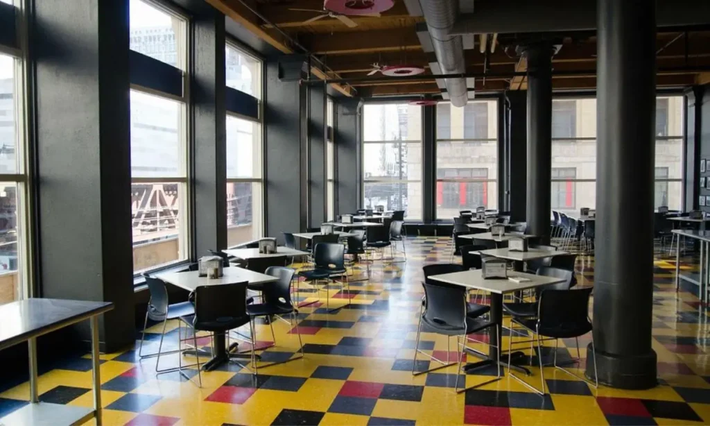 A spacious dining area at HI Chicago Hostel with large windows, black chairs, and colorful tiled floors.