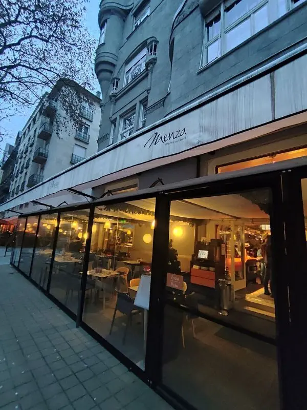 The exterior of Menza restaurant at dusk with warm lights inside.