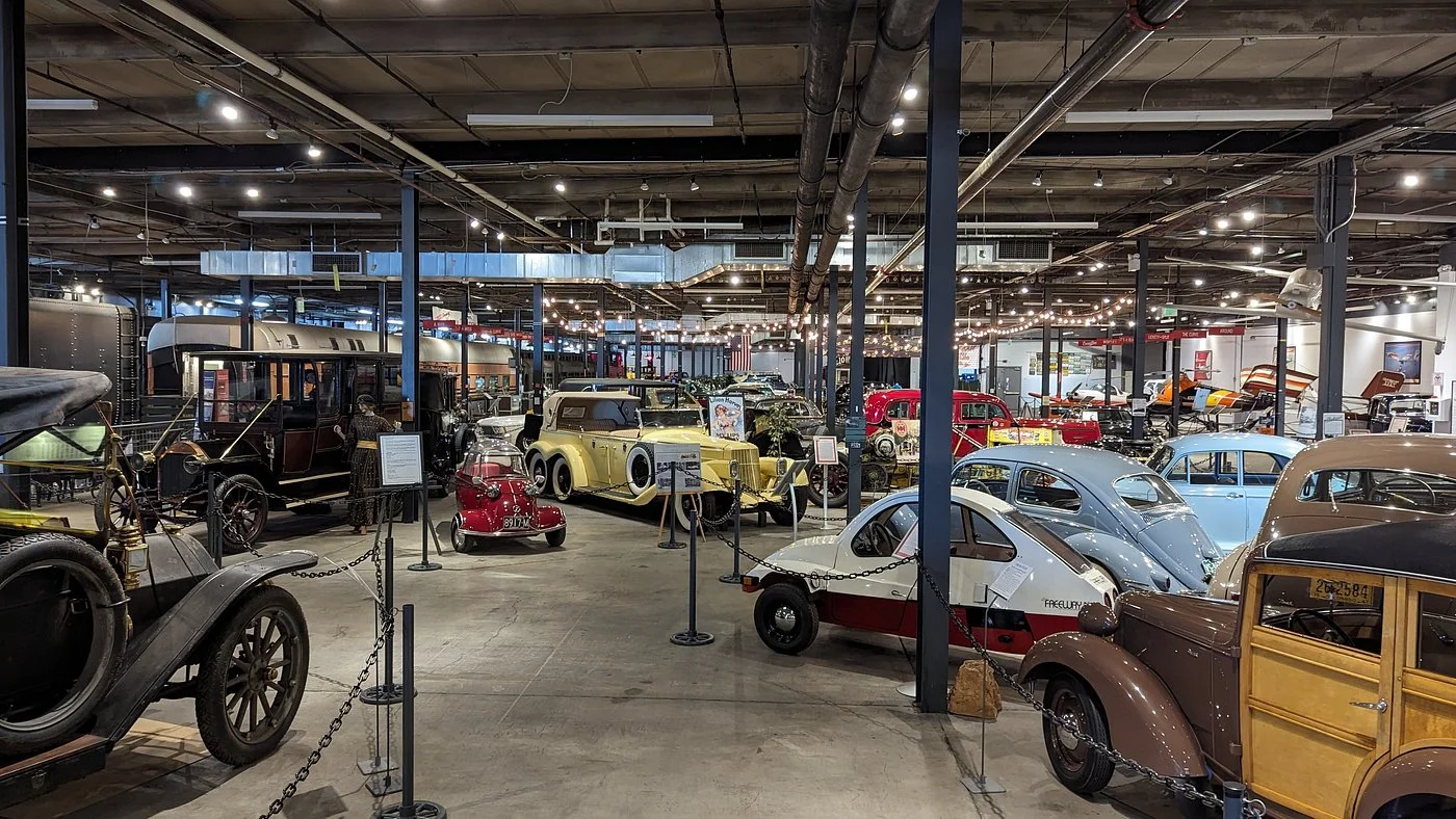 Interior view of Forney Museum showing vintage cars displayed on concrete floors under industrial warehouse lighting with exposed ceiling beams and columns