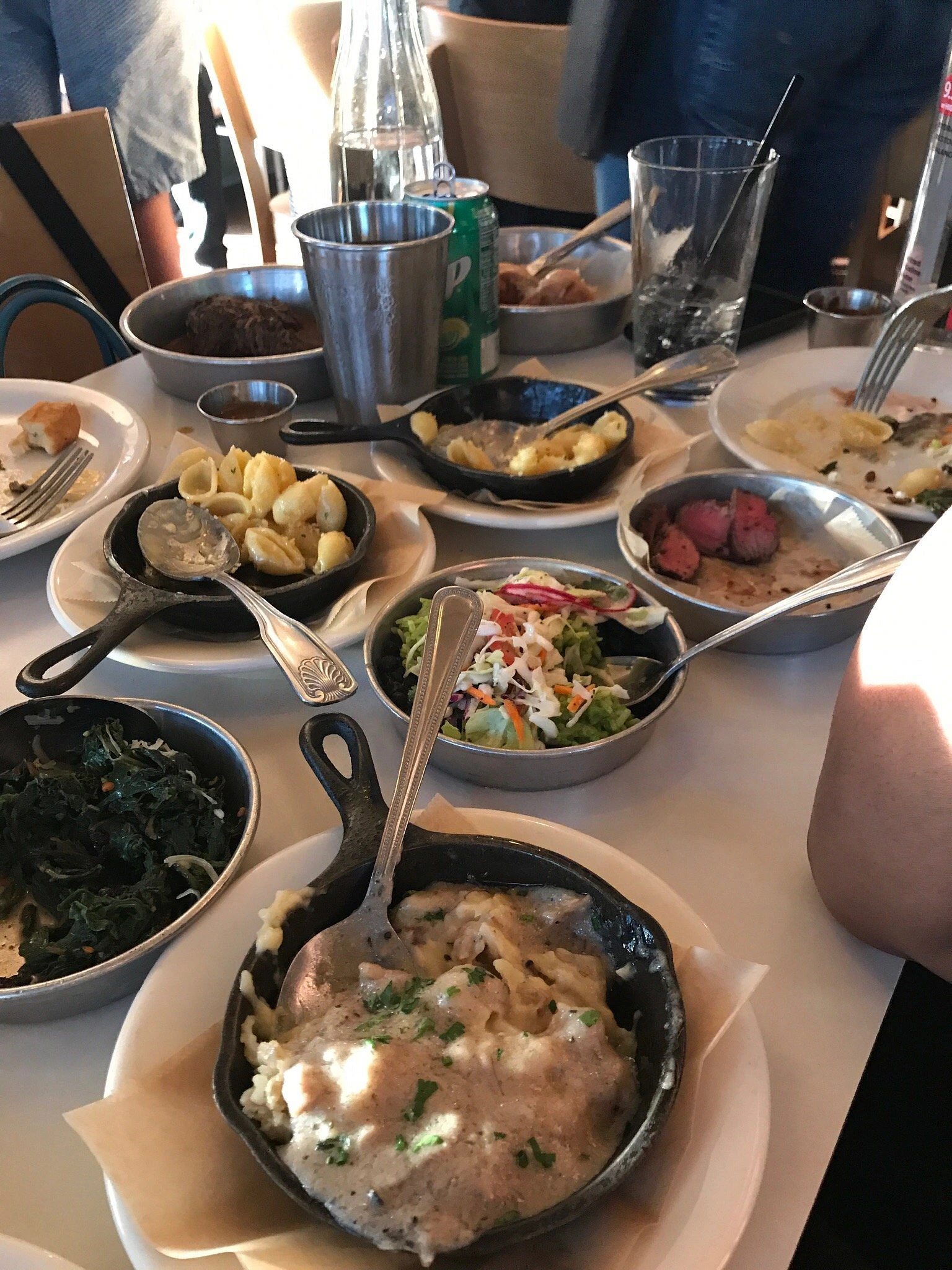 Multiple small plates and cast iron skillets filled with Latin American dishes including wood-fired octopus, greens, and various shared appetizers on a restaurant table at Work & Class Denver