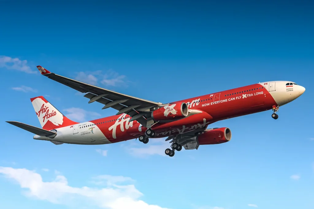 Red and white AirAsia X Airbus A330 airplane landing against a blue sky with scattered clouds