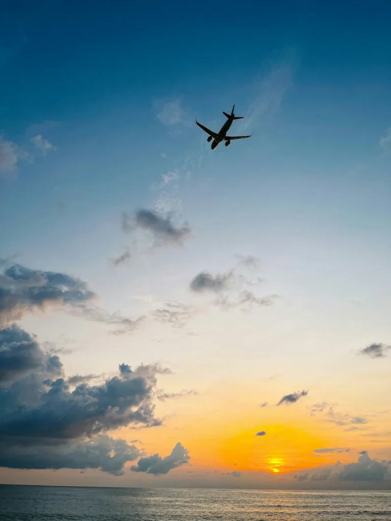 Silhouetted passenger airplane flying high above the ocean against a vibrant orange and blue sunset sky