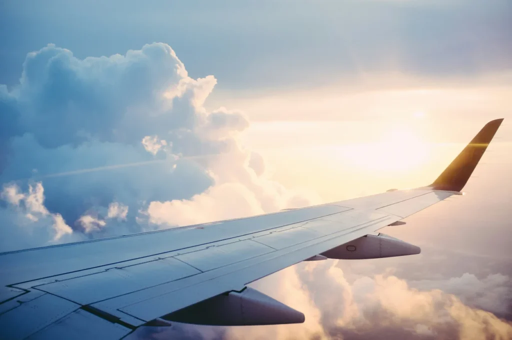 View of an airplane wing flying through soft clouds at sunset