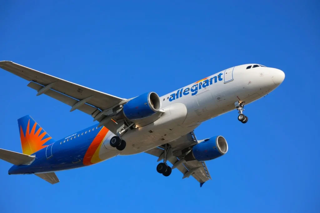 An Allegiant Air Airbus A320 flying overhead with its landing gear deployed against a blue sky