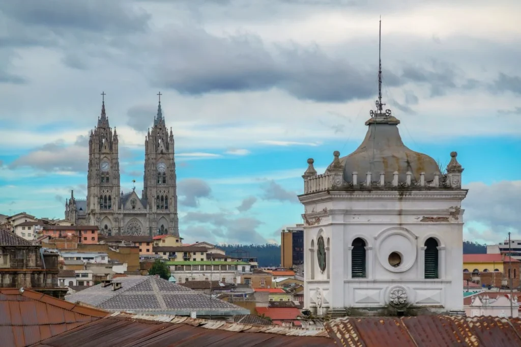 The Basilica of the National Vow rising above rooftops and an old white bell tower in Quito