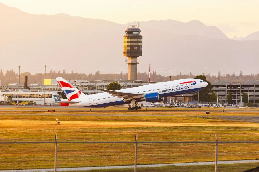 British Airways Boeing 777 takes off from Vancouver Airport at sunset with mountains in the background