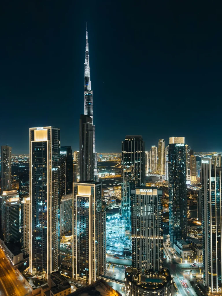 The lit-up Burj Khalifa skyscraper surrounded by modern high-rise buildings in downtown Dubai at night
