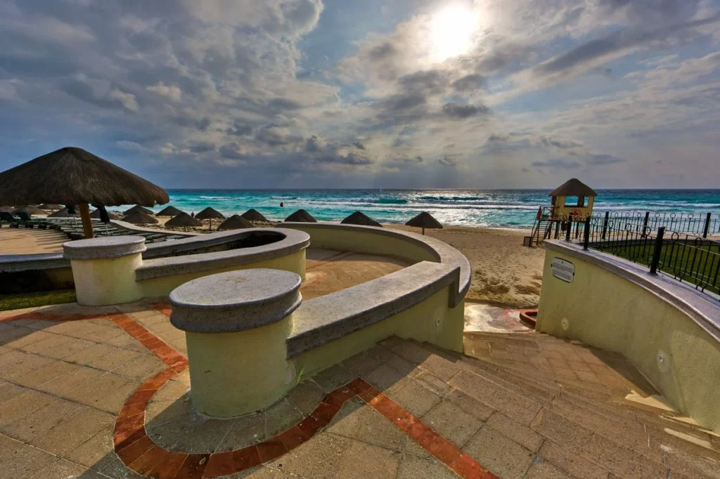 Stone patio overlooking a sandy beach with thatched umbrellas and turquoise water in Cancún
