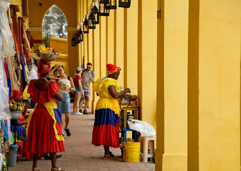 Palenqueras in traditional dresses standing under the yellow arches of Las Bóvedas in Cartagena, Colombia