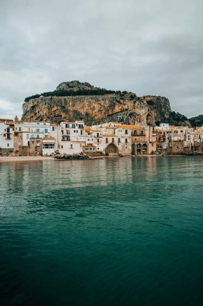 Waterfront view of historic stone buildings in Cefalù, Sicily below a steep cliff