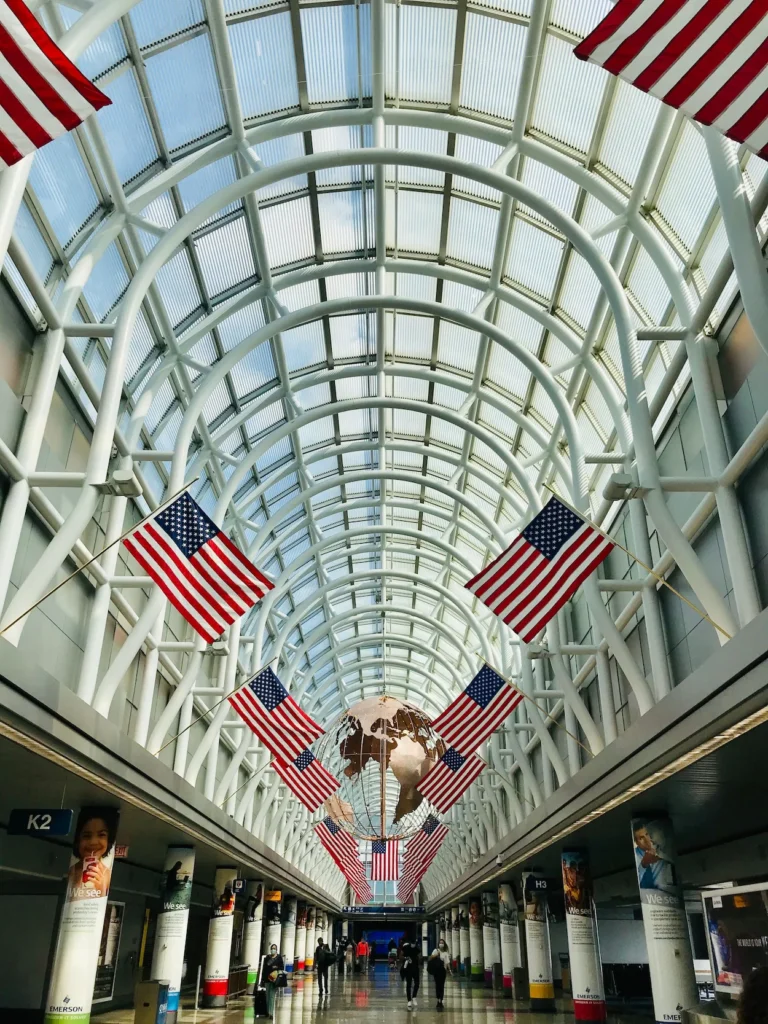 American flags hang above the wide pedestrian concourse under a vaulted glass ceiling at O'Hare Airport