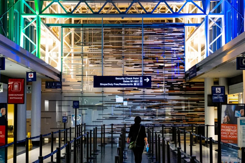 A passenger walks toward an O'Hare Terminal 5 security line below bright blue and green lights
