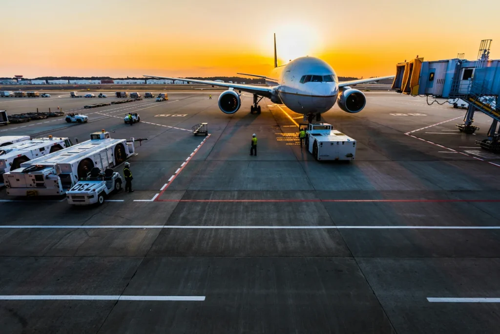 An airplane parked at a terminal gate during a bright sunset on the tarmac