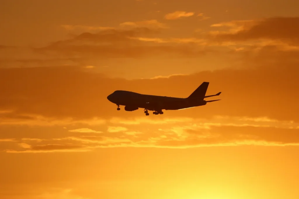 Silhouette of a commercial airplane flying through an orange sunset sky
