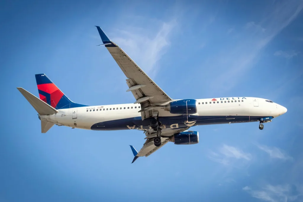 A Delta Air Lines Boeing 737-800 passenger jet descending with its landing gear down against a bright blue sky