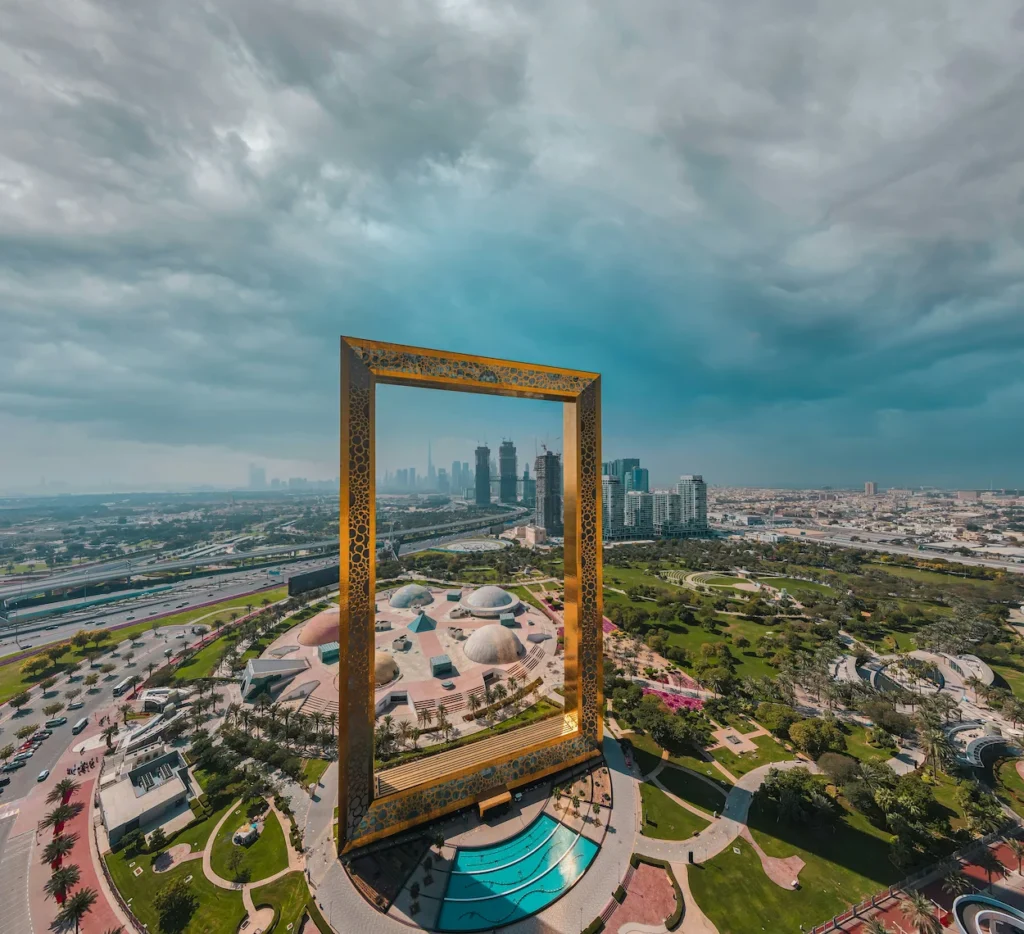Aerial view of the golden Dubai Frame structure in Zabeel Park under a dramatic cloudy sky
