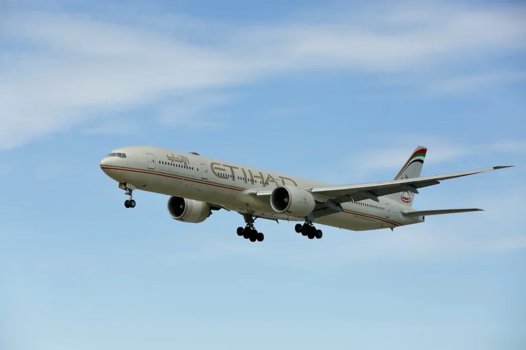 Etihad Airways Boeing 777 airplane flying with landing gear down against a cloudy blue sky