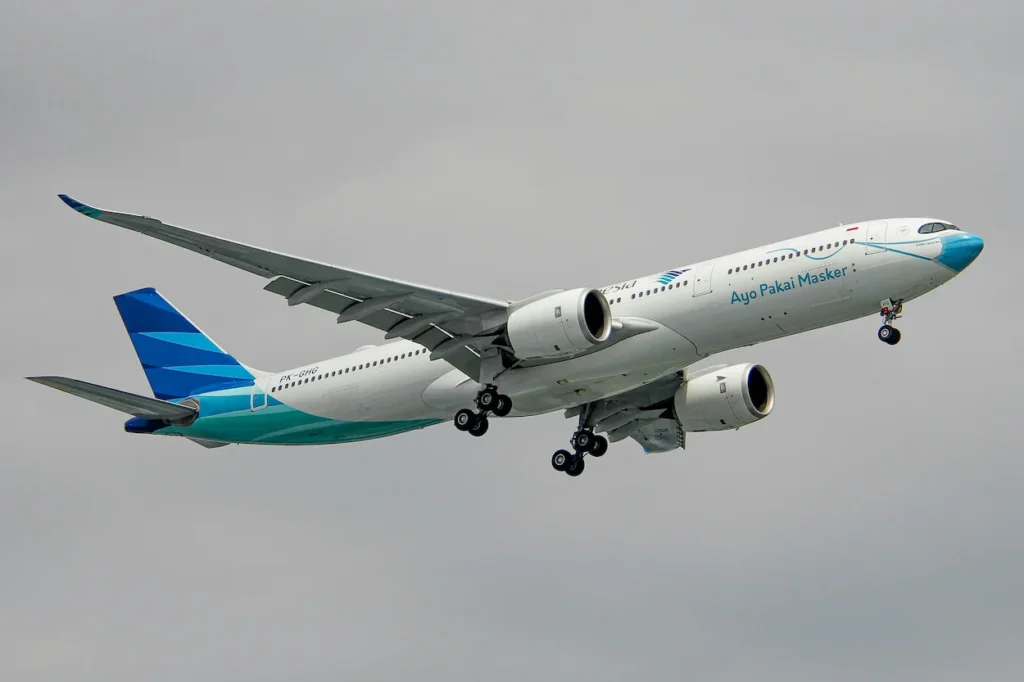 Garuda Indonesia Airbus A330neo airplane flying with landing gear down against an overcast sky