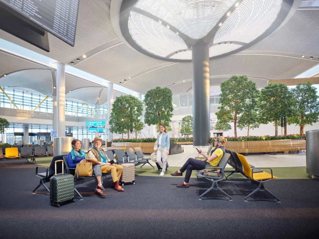 Passengers relaxing in a modern airport terminal seating area surrounded by indoor trees
