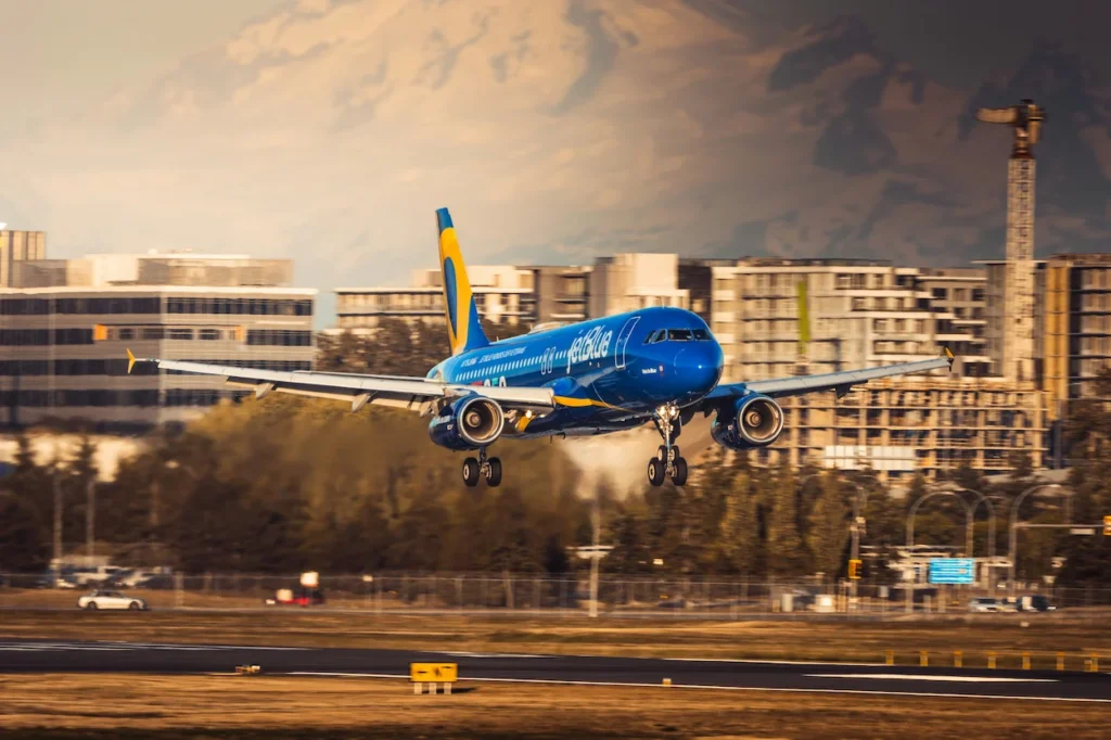 JetBlue Airbus A320 plane touching down on a runway with city buildings and mountains behind
