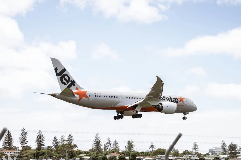Jetstar Boeing 787 Dreamliner airplane landing over trees under a cloudy sky