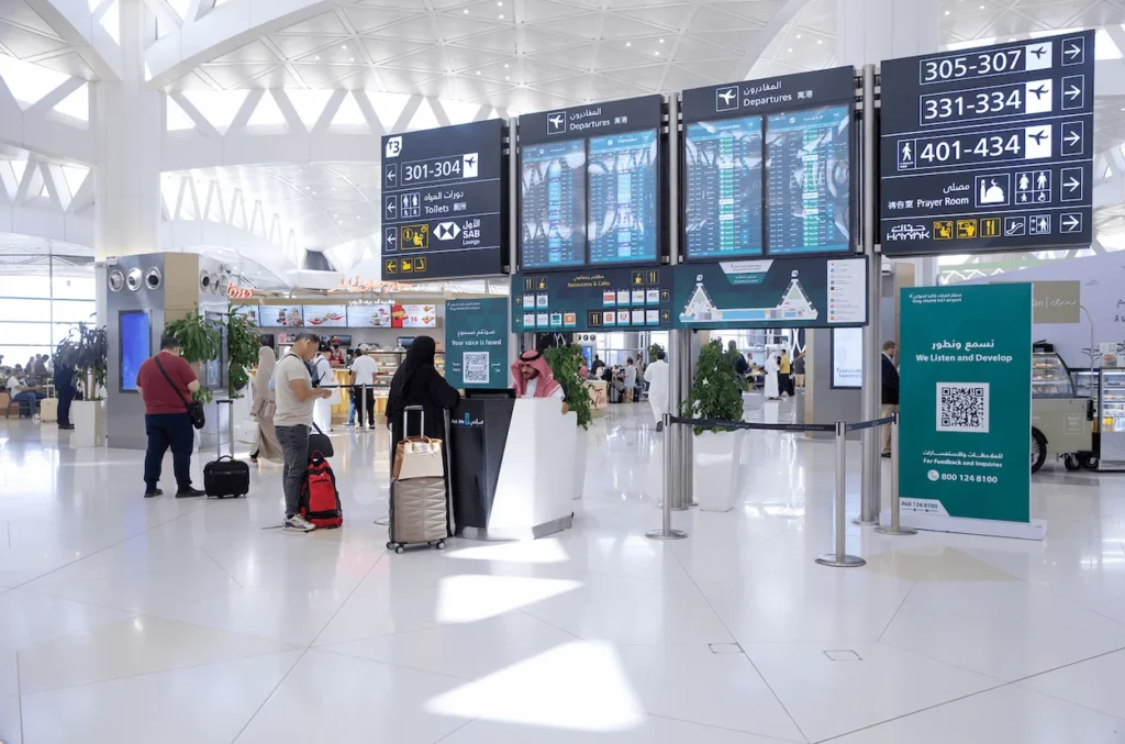 Passengers checking large digital departure flight information screens inside an airport terminal