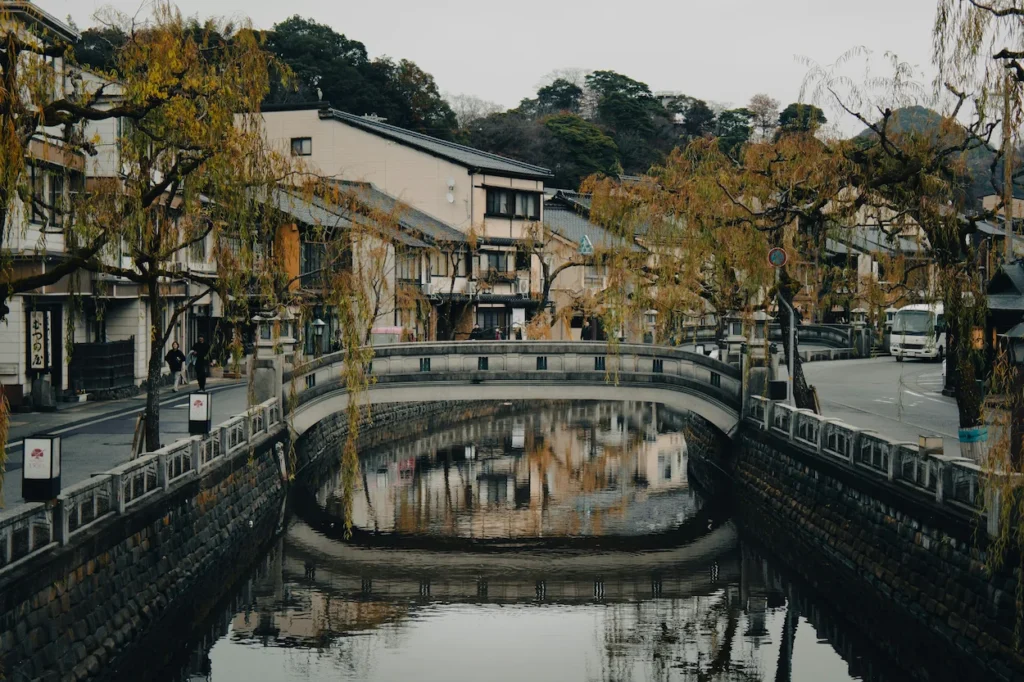 Stone bridge over a calm canal lined with willow trees and traditional buildings in Kinosaki Onsen