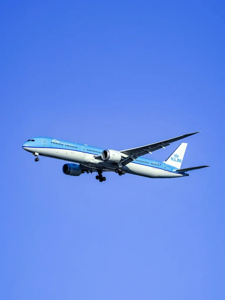 A KLM Boeing 787 Dreamliner descends for landing against a solid blue sky backdrop
