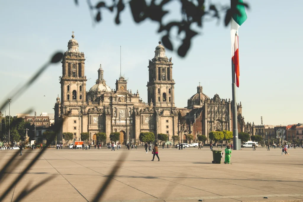 Mexico City Metropolitan Cathedral viewed across the open Zócalo plaza with a Mexican flag flying on the right