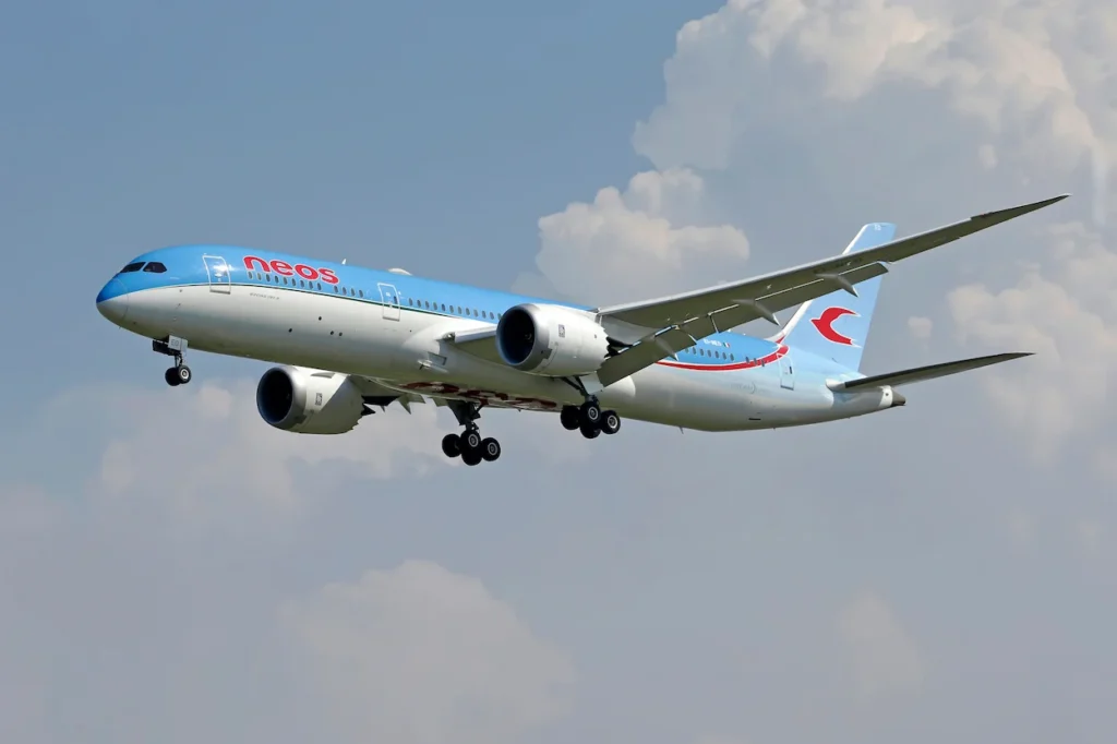 Neos Airlines Boeing 787-9 Dreamliner airplane flying with landing gear extended against a cloudy sky