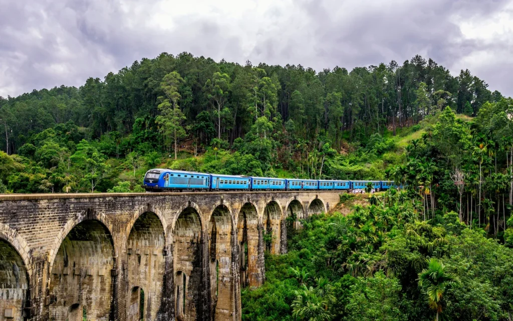 A blue passenger train crossing Nine Arch Bridge in Ella Sri Lanka