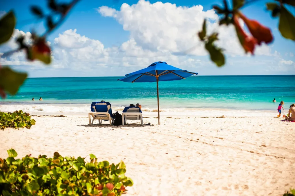 Lounge chairs under a blue umbrella on a white sand beach in Ocho Rios, Jamaica