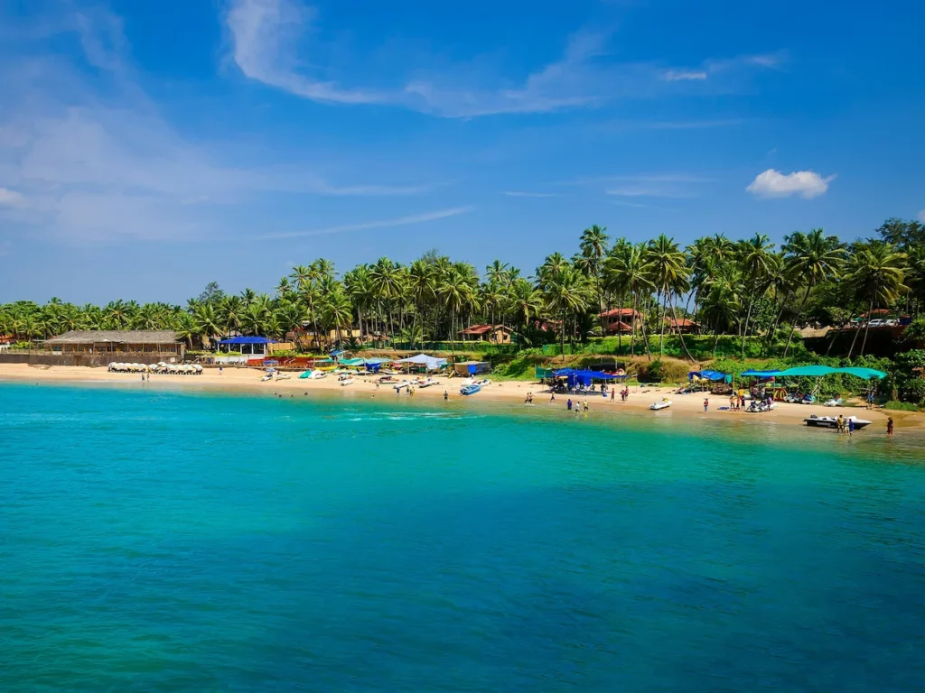 A bright turquoise sea framing a sandy shore lined with palm trees and beach shacks at Palolem Beach in Goa