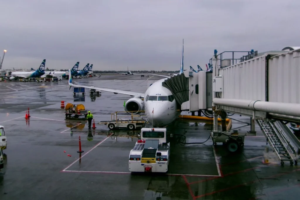 An Alaska Airlines plane parked at an airport gate on a rainy tarmac