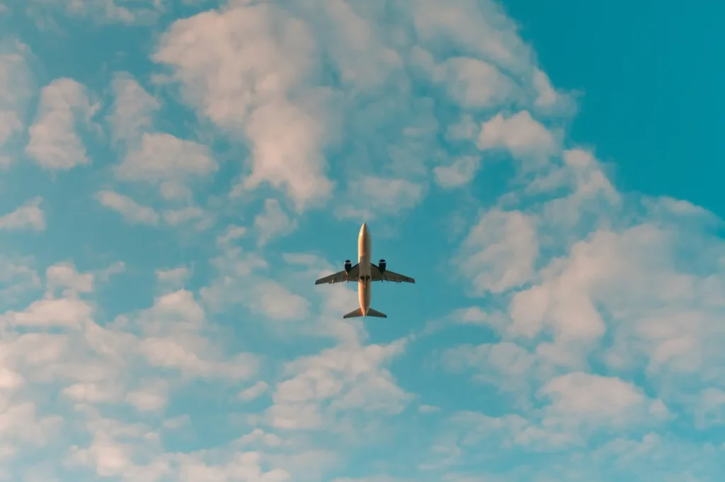 Low-angle view of a commercial airplane flying overhead through a blue sky filled with white clouds