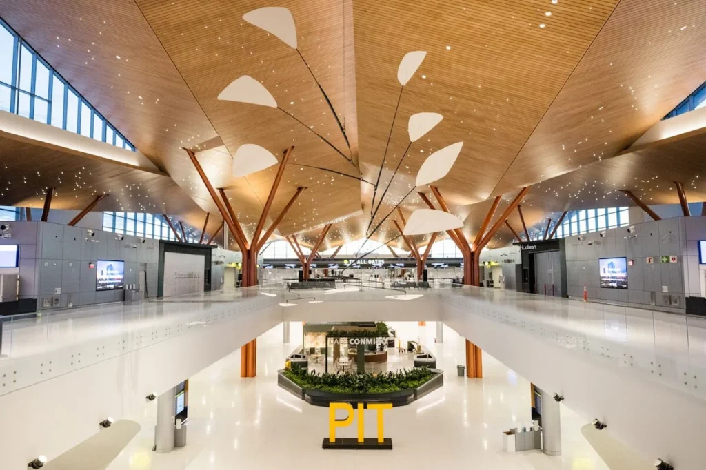 A large "PIT" sign sits in the modern, wood-ceilinged atrium of Pittsburgh International Airport
