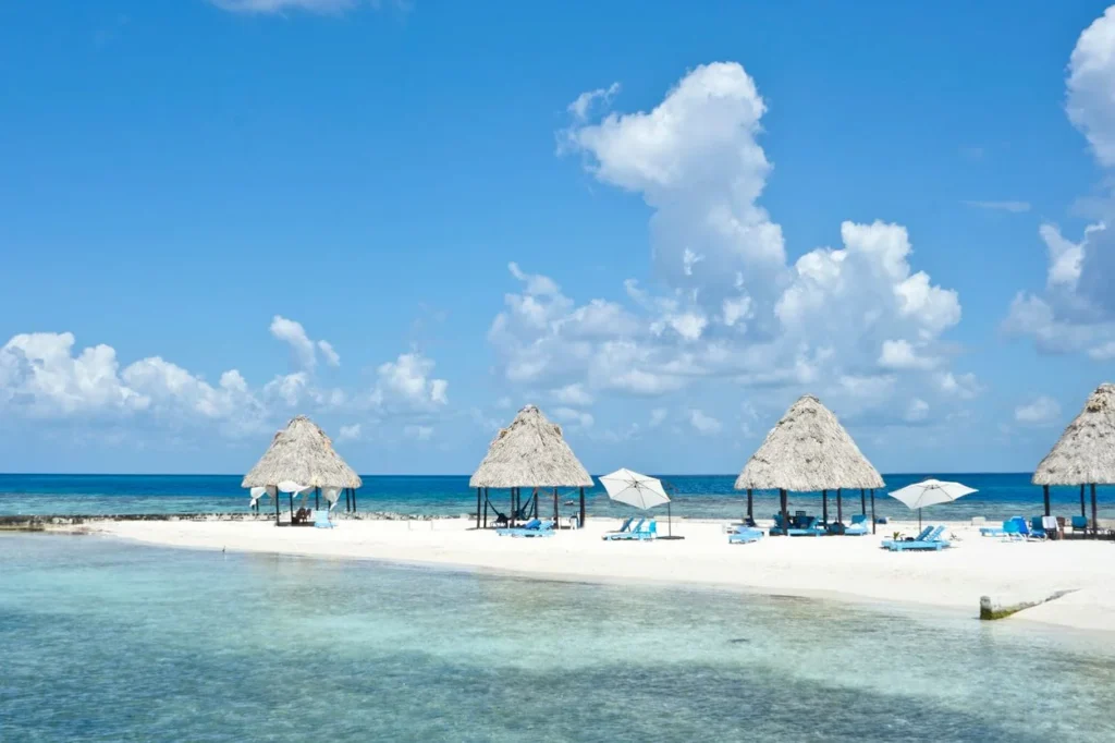 Thatched palapas on the white sand beach of Rendezvous Caye in Belize