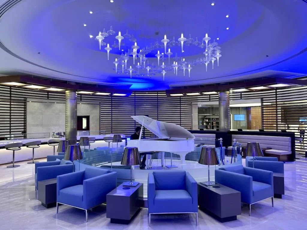 A white grand piano and blue armchairs in the Alfursan Lounge