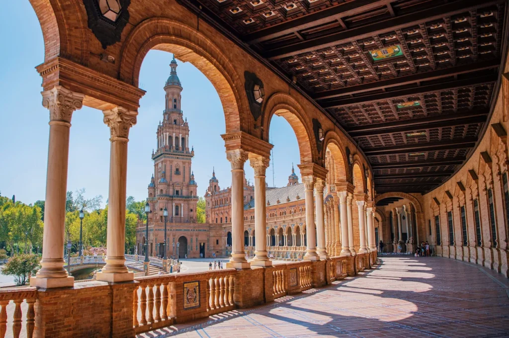 Ornate columned arcade looking out toward the North Tower of the historical Plaza de España in Seville, Spain