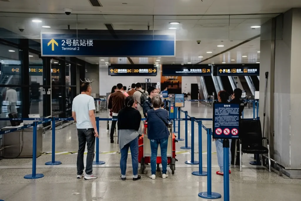 Passengers waiting in a queue line below a blue Terminal 2 directional sign