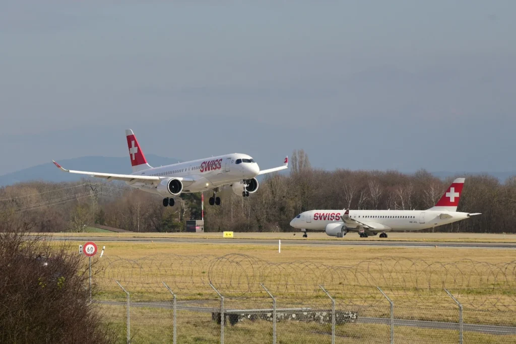 One SWISS Airbus A220 jet touches down on the runway while another waits nearby on the taxiway