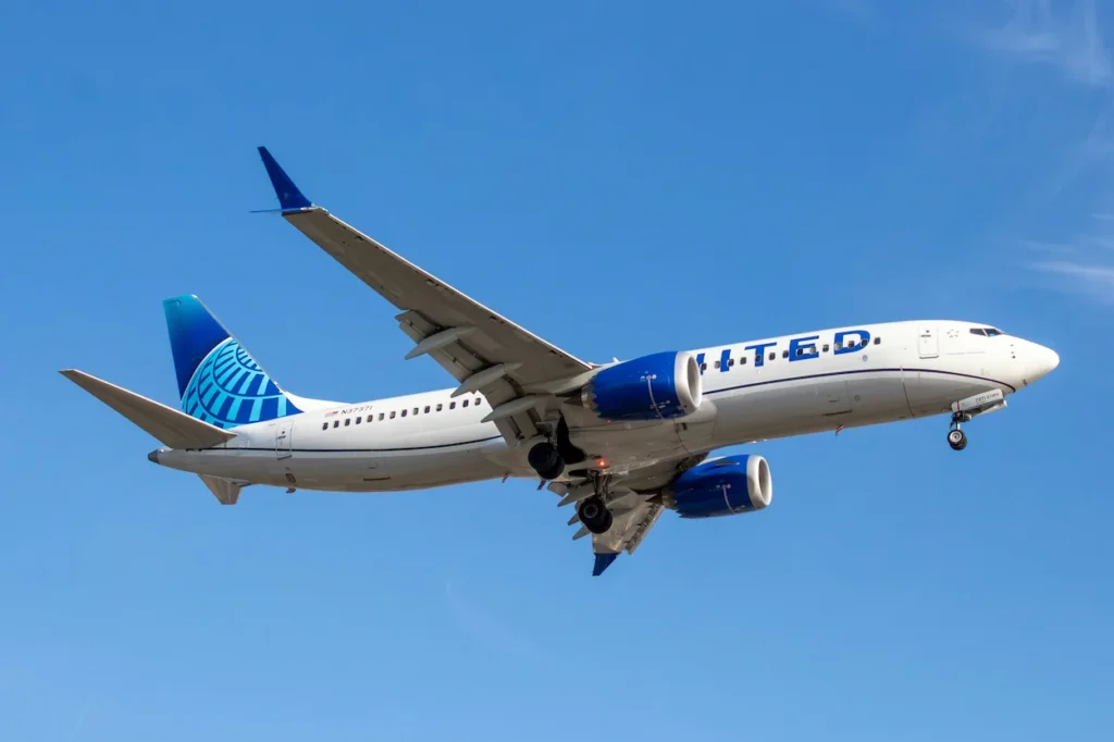 A United Airlines Boeing 737 MAX 8 airplane descending with its landing gear down against a clear blue sky