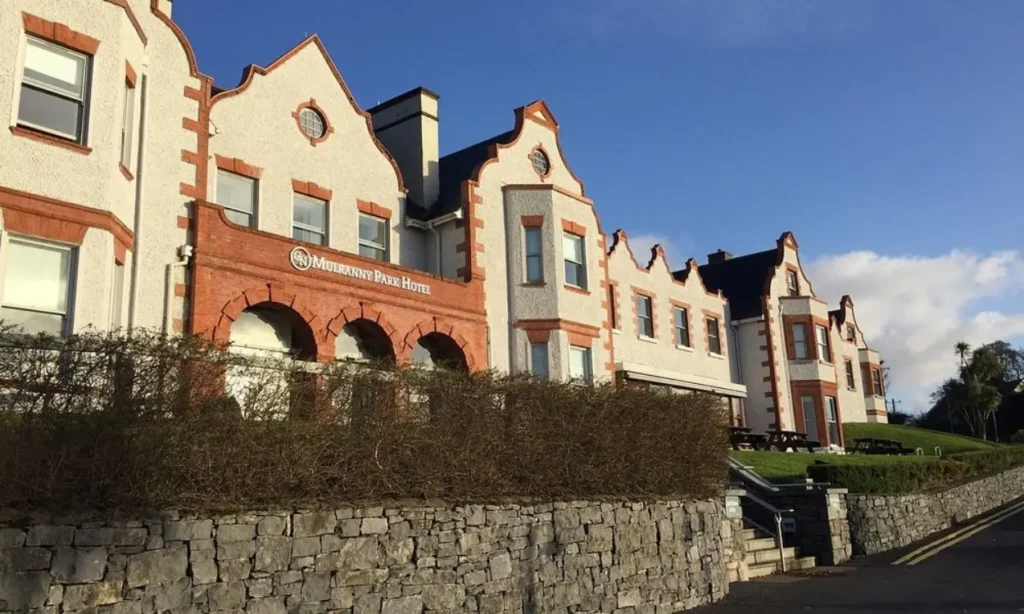 The white and red building of Mulranny Park Hotel stands under a clear blue sky.